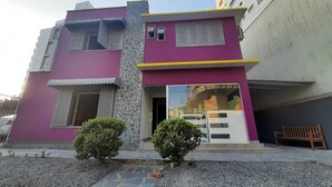 Una casa de dos plantas con fachada morada, un pilar de piedra y un pequeño jardín delantero con dos arbustos.