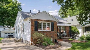 Une maison de plain-pied avec une façade en briques, une véranda couverte avec des sièges d’extérieur et un garage.
