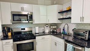 Une cuisine moderne avec des meubles blancs, des appareils en acier inoxydable, un four à micro-ondes, une cuisinière et un grille-pain.