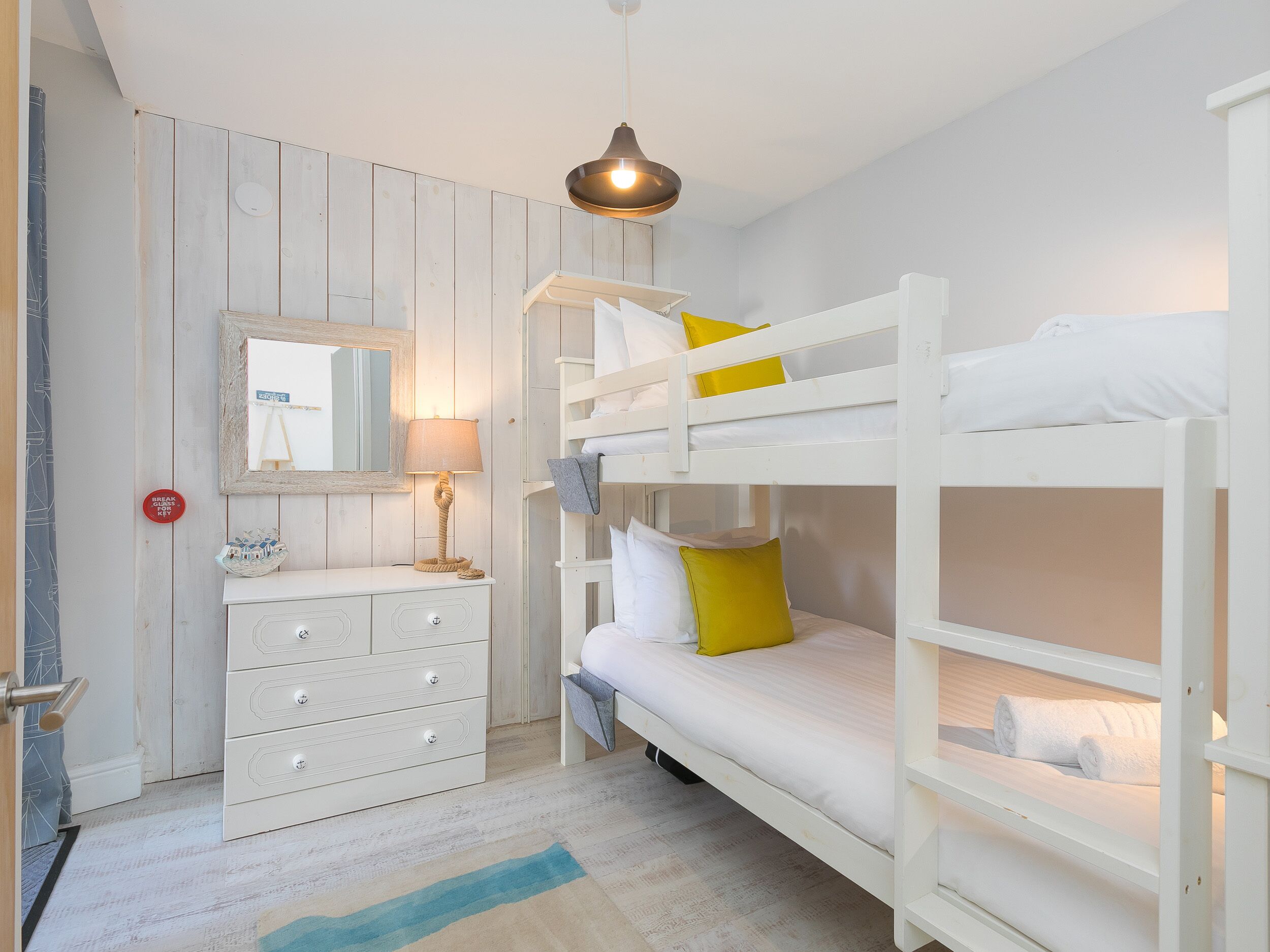 Une chambre avec un lit superposé, une commode, un miroir et une lampe suspendue.