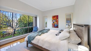 A modern bedroom with a large window, a bed with white linens, a blue throw blanket, and a wooden headboard. - Broadwater Waves family home, short walk to beach (Cape Woolamai)