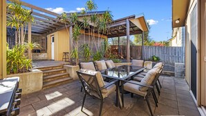 A patio area with a glass-top table and chairs, surrounded by potted plants and a wooden fence. - Broadwater Waves family home, short walk to beach (Cape Woolamai)