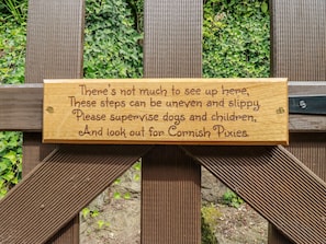 A wooden sign with a warning about uneven steps and a request to supervise dogs and children.