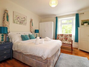 A bedroom with a bed, a nightstand, a dresser, a chair, and a window with curtains. - Vis Valley View (St Austell)