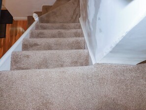 Una escalera alfombrada con barandilla y pared blancos.