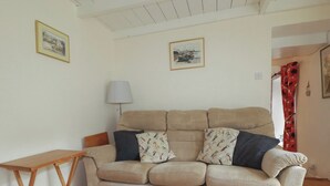 Uma sala de estar com um sofá bege, uma mesa lateral de madeira e duas molduras com imagens na parede.