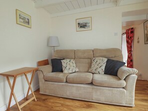 A living room with a beige sofa, a wooden side table, and two framed pictures on the wall.