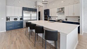 Une cuisine moderne dotée d’un grand îlot central, de meubles bleu foncé, d’appareils électroménagers en acier inoxydable et d’un dosseret en marbre blanc.