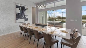 Un espace repas moderne, doté d’une grande table, de chaises et offrant une vue sur l’extérieur.