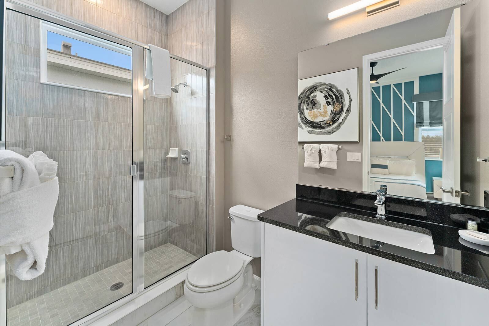 A modern bathroom with a glass-enclosed shower, a white toilet, a black countertop, and a large mirror.