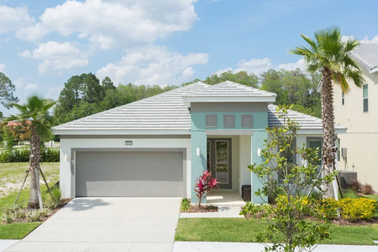 A single-story house with a garage, a front porch, and a small garden with palm trees and shrubs.