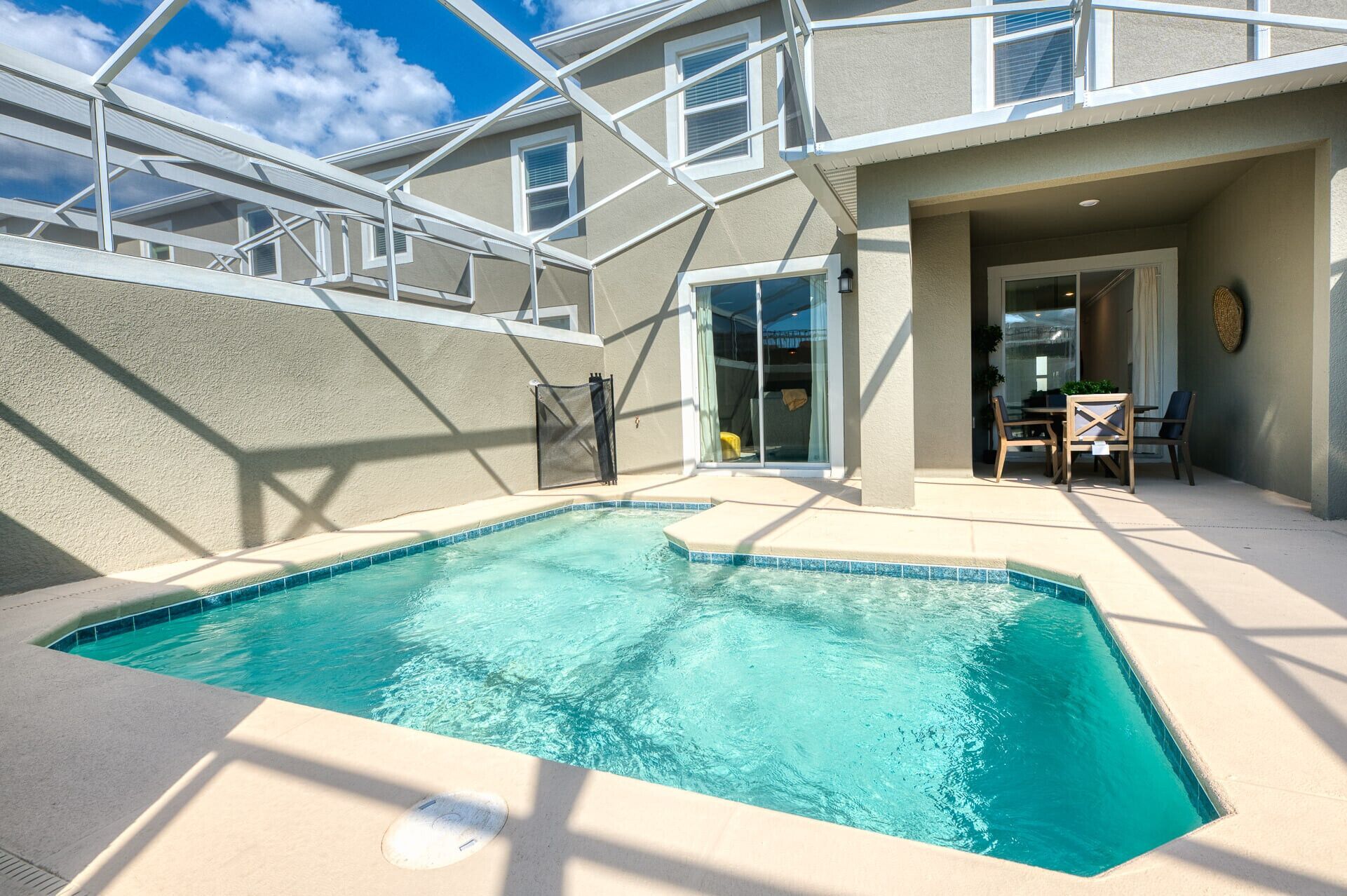 A swimming pool with a clear blue water, surrounded by a covered patio area with a table and chairs.