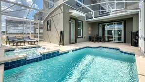 Une piscine entourée de parois en verre, des chaises longues et un espace extérieur aménagé avec une table et des chaises.