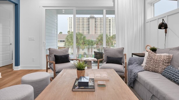 Ein modernes Wohnzimmer mit Couchtisch aus Holz, zwei grauen Sofas und einem großen Fenster mit Blick auf hohe Gebäude und Palmen.