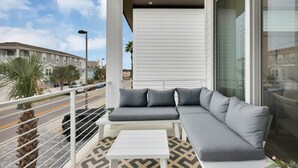 Ein Balkon mit einer grauen Couch, einem kleinen weißen Tisch und einem Fußboden mit Muster.