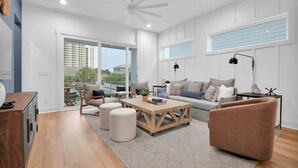 Ein geräumiges Wohnzimmer mit Couch, Zweisitzer und einem Holztisch. Eine Deckenventilator, eine Stehlampe und ein Fenster mit Jalousien sind ebenfalls vorhanden.