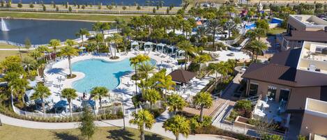 An aerial view of a resort with a central swimming pool, multiple lounge areas, and a lake in the background.