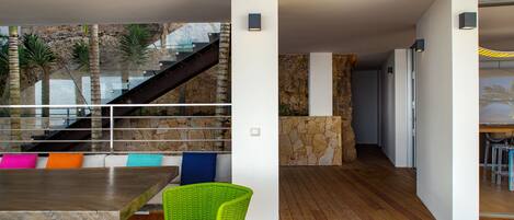 A modern interior with a wooden floor, a staircase, and a dining area with colorful cushions.