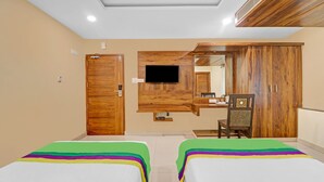Quarto de hotel com duas camas, um guarda-roupa de madeira, uma televisão na parede e um espelho sobre o guarda-roupa.