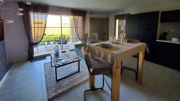 A modern dining area with a table set for two, a sofa, and a view of the outdoors. - Charming love room Althea (Fontenay-le-Comte)