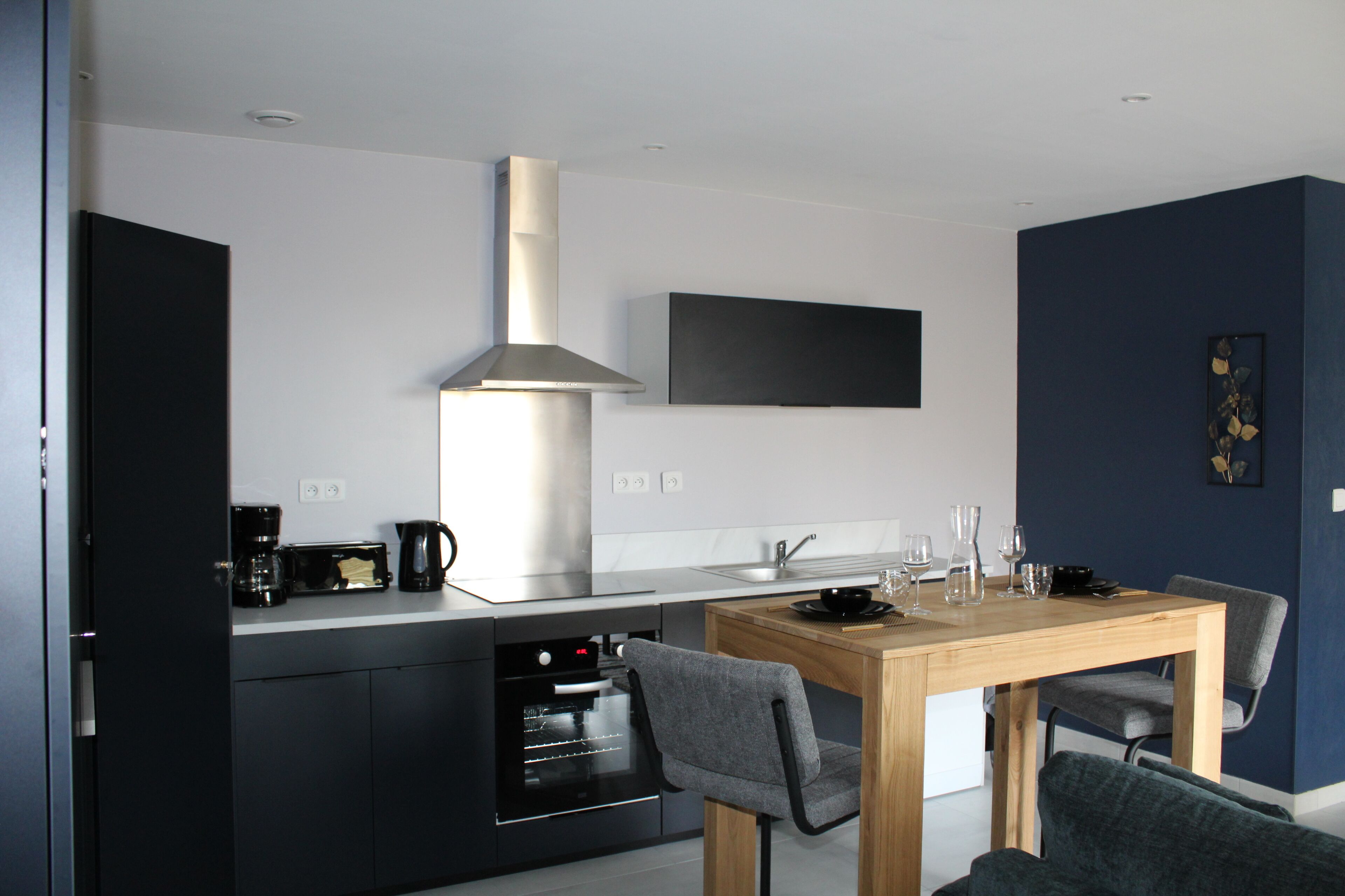 A modern kitchen with a built-in oven, a coffee maker, and a dining area with a wooden table and chairs.
