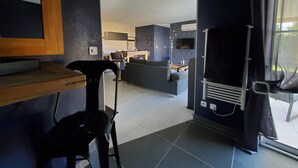 A modern living room with a sofa, a dining table, and a kitchen area in the background. - Charming love room Althea (Fontenay-le-Comte)