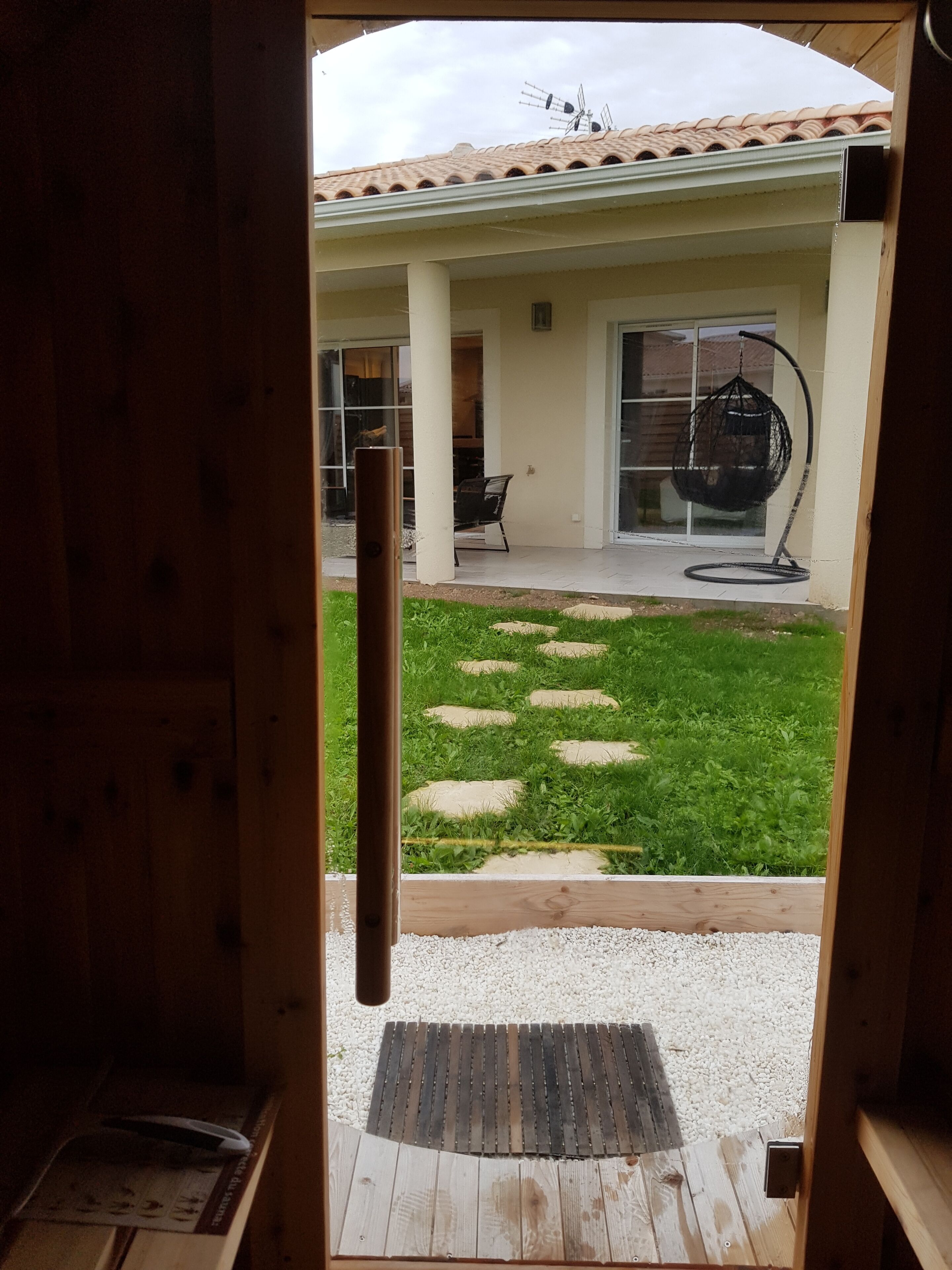 A wooden door leading to a patio with a tiled roof, a hanging chair, and a stone pathway.