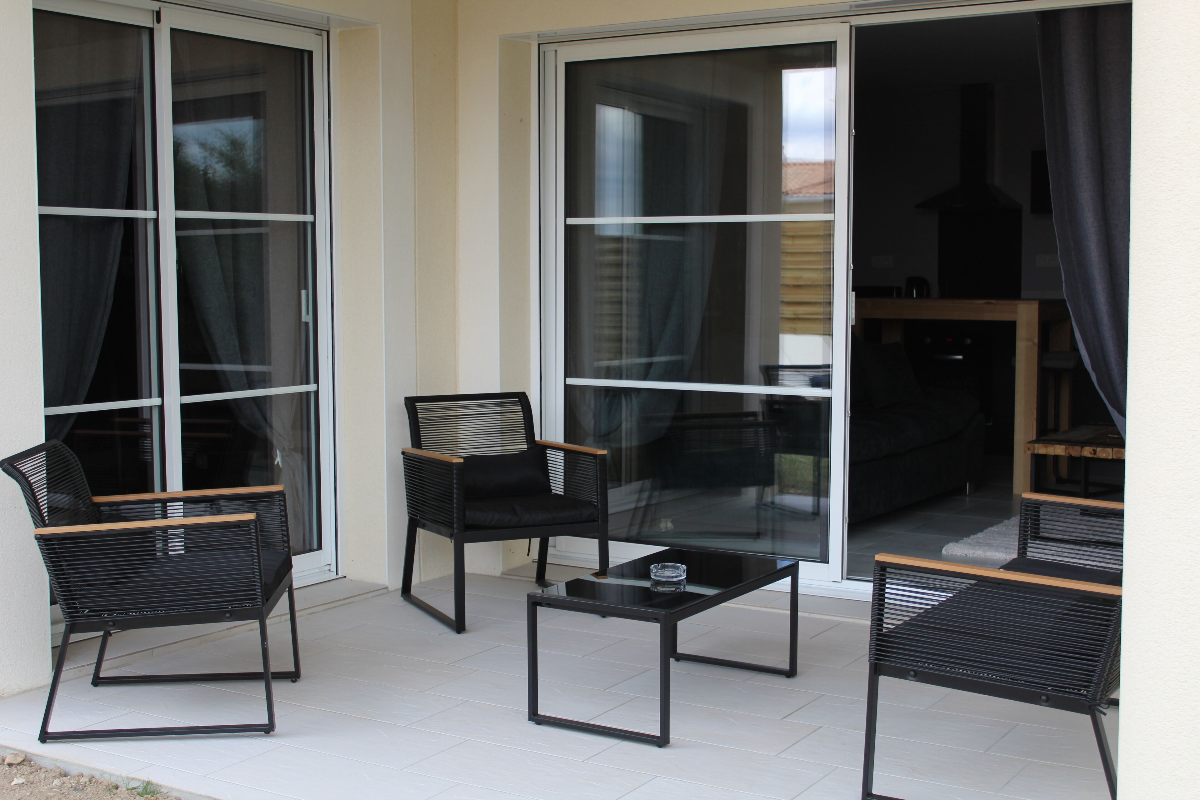 Un balcone con due sedie nere, un tavolino e una porta scorrevole con vista sull'esterno.