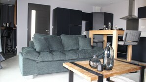 A modern living room with a grey sofa, a wooden coffee table, and a dining area with a wooden table and chairs. - Charming love room Althea (Fontenay-le-Comte)