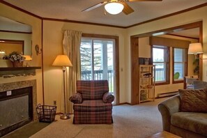 A cozy living room with a fireplace, a plaid armchair, and a ceiling fan. - 2107  Pool, Hot tub, sauna & much more! The Knotty Pine (Beech Mountain)