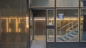 Ein moderner Hauseingang mit Glastür, Treppe und Metallgeländer.