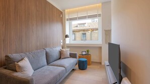 Ein stilvolles Wohnzimmer mit einer grauen Couch, einem Fernseher und einem Fenster mit Jalousien.