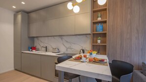 Eine moderne Küche mit grauen Schränken, einer Marmor-Spritzschutzwand und einem Essbereich mit einem weißen Tisch und zwei schwarzen Stühlen.