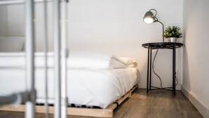 A minimalist bedroom with a bed, a bedside table with a lamp, and a potted plant.