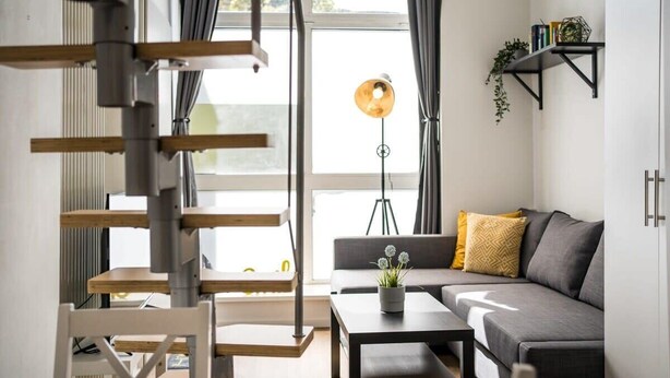 A modern living room with a gray sofa, a coffee table, and a floor lamp. There is a staircase with wooden steps and metal railings.