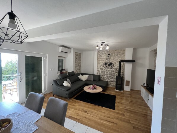 A modern living room with a wooden floor, grey sofa, and a dining area with a table and chairs. - Villa with heated pool, sea view - a few minutes from the beach (Podgora)