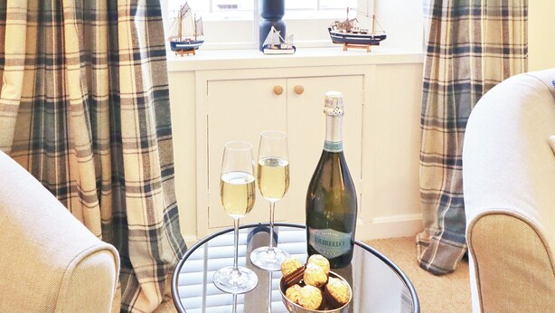 A glass table with two wine glasses, a bottle of wine, and a bowl of chocolates. - 2 bedroom accommodation in Kirkcudbright (Kirkcudbright)