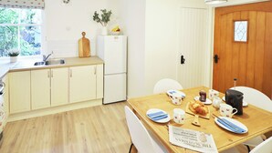 A compact kitchen with a wooden table set for breakfast, white cabinets, and a refrigerator. - 2 bedroom accommodation in Kirkcudbright (Kirkcudbright)