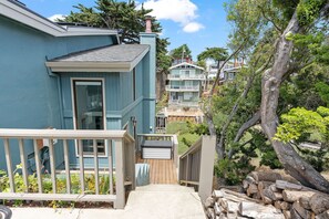 Two-story house with a front deck and a large tree in a residential neighborhood.