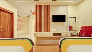A hotel room with two single beds, a desk with a chair, a TV, a mirror, and a wardrobe. - Itsy Hotels Sri Sai Grand Inn (Vijayawada)