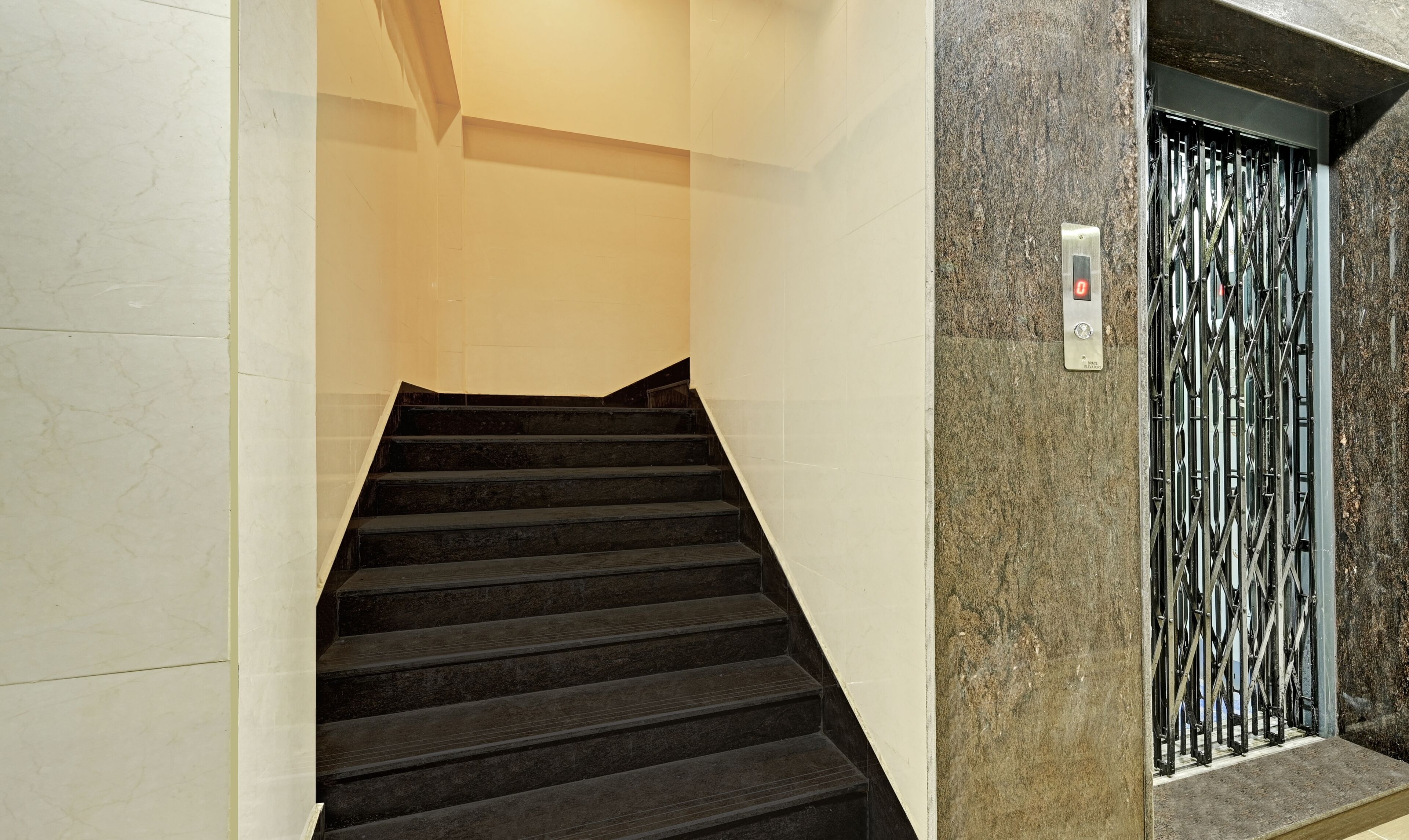 A staircase with black steps leading up to a metal elevator door with a red light.