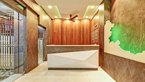 A reception area with a wooden panel wall, a ceiling fan, and a reception desk. - Itsy Hotels Sri Sai Grand Inn (Vijayawada)