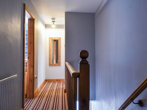 Um corredor com piso de madeira, porta de madeira, espelho e ventilador de teto.