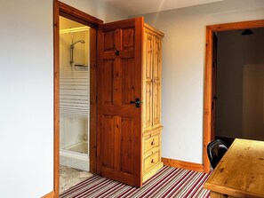 A room with a wooden wardrobe, a bathroom with a shower, and a striped carpet. - Tom Wragg Suite - UK40248 (Bakewell)