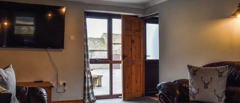 A cozy living room with a leather sofa, a wooden door leading outside, and a flat-screen TV mounted on the wall.