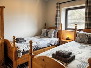 A bedroom with two wooden beds, a nightstand with a lamp, and a window with curtains.