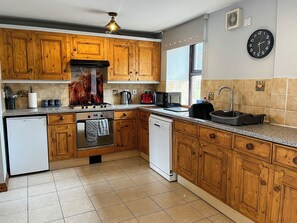 A kitchen with wooden cabinets, a stove, a sink, and a clock on the wall. - Tom Wragg Suite - UK40248 (Bakewell)