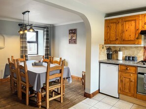 A dining area with a table and chairs, a kitchen with wooden cabinets, and a window with curtains.