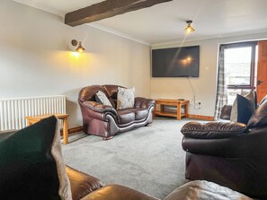 A living room with a brown leather sofa, a wooden coffee table, and a flat-screen TV mounted on the wall.