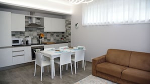 Une cuisine moderne avec des meubles blancs, une table à manger avec des chaises et un canapé marron dans l’espace salon.
